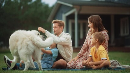 Wall Mural - Portrait of a Happy Young Family Couple with a Son and Daughter, and a White Golden Retriever Sitting on a Grass in Their Front Yard at Home. Cheerful People Petting and Playing with Dog.