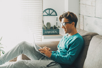 Happy teenager at home using laptop sitting comfortably on the sofa alone at home. Student lifestyle day activity for remote class with computer and internet wireless connection. Modern education