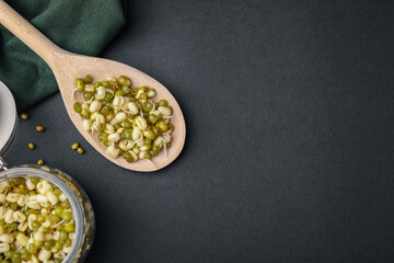 Wooden spoon with sprouted green mung beans on black background, flat lay. Space for text