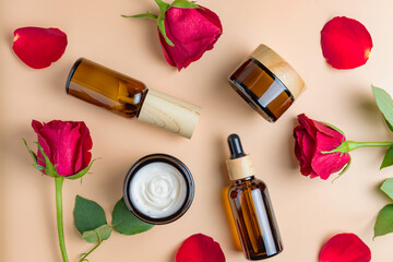 Set of natural organic SPA beauty products on beige background with red roses and petals. Homemade rose face oil, moisturizer cream jar, amber glass spray bottle on beige background