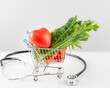 Health care still life with organic vegetables in a shopping cart with decorative heart and stethoscope on a white table. Concept of healthy food and control of good health with a diet