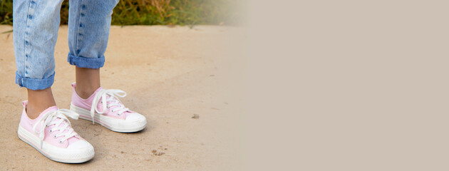 A view of the legs of a teenage girl in pink sneakers and blue jeans against a background of yellow dry grass. The concept of clothing for modern teenagers in the cool season.