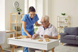 © Studio Romantic - Smiling young female social worker and old man playing with jigsaw puzzle in nursing home. Caregiver in medical uniform helps elderly man to put together puzzles and letters. Old age concept.