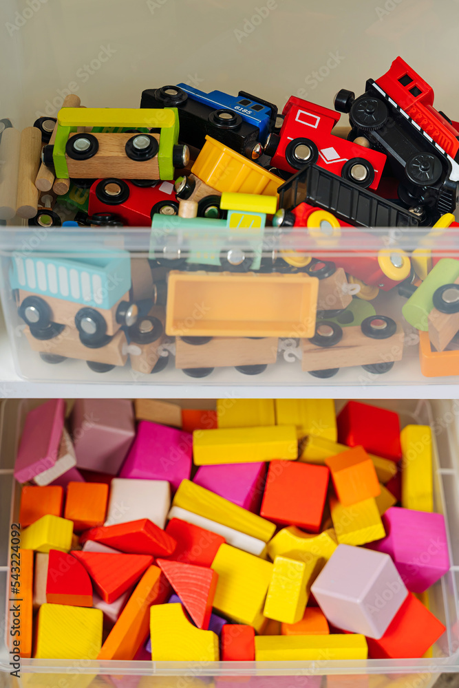 Transparent plastic storage boxs on shelves. White shelving with rainbow wooden toys in plastic containers. Toys sorting system. Organizing and storage ideas in nursery.