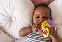 Close-up Portrait Of Cute Black Baby On Pillows Gnawing Toy