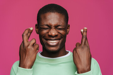 Black young man smiling and holding fingers crossed for good luck