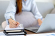 © Katcha - Female freelance is typing to search data on laptop and writing information on notebook while sitting