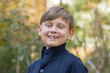 Street portrait of a smiling 10-year-old boy on a blurry background of nature. One front tooth is missing.