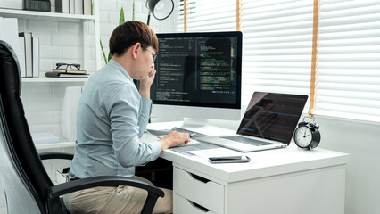 Male programmer is programming to develop program app and website of corporate while working to checking program code and debugging on multiple screen at modern software office