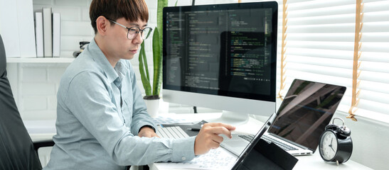 Male programmer is programming to develop program app and website of corporate while working to checking program code and debugging on multiple screen at modern software office