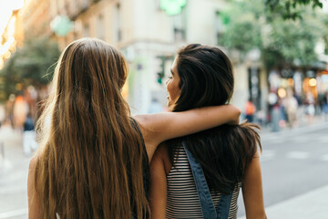 Rearview of a blonde female putting her arm around her friend's neck.