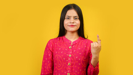 Young Indian girl showing finger after voting, cheerful girl isolated over yellow background