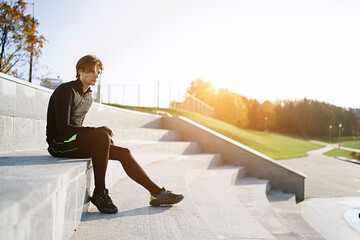 Wall Mural - Man sitting on the steps after taking a break from morning jogging with city background. Healthy lifestyle concept sit on the steps