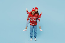 Full Body Merry Young Couple Two Man Woman Wear Red Christmas Sweater Santa Hat Posing Give Piggyback Ride To Joyful Sit On Back Isolated On Plain Blue Background. Happy New Year 2023 Holiday Concept.