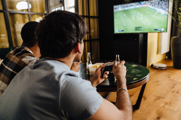 Canvas Print - Back view of young male friends playing football video game with gamepads at home