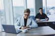 © Дмитрий Ткачук - A female manager is sitting at a desk using a laptop in a modern office against the background of a colleague. Working atmosphere in the office.