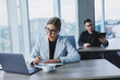 © Дмитрий Ткачук - A female manager is sitting at a desk using a laptop in a modern office against the background of a colleague. Working atmosphere in the office.