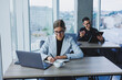 © Дмитрий Ткачук - A female manager is sitting at a desk using a laptop in a modern office against the background of a colleague. Working atmosphere in the office.