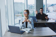 © Дмитрий Ткачук - A female manager is sitting at a desk using a laptop in a modern office against the background of a colleague. Working atmosphere in the office.