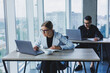 © Дмитрий Ткачук - Working atmosphere in an office with large windows. A female manager is sitting at a desk using a laptop in a modern office against the background of a colleague.