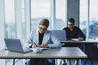 © Дмитрий Ткачук - Working atmosphere in an office with large windows. A female manager is sitting at a desk using a laptop in a modern office against the background of a colleague.