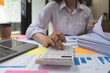 © Natee Meepian - accounting concept. businesswoman working using calculator with money stack in office