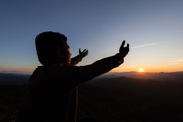 silhouette of a man Praying hands with faith in religion and belief in God On the morning sunrise background.  Prayer position.