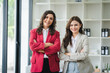 © Daenin - Two female designers smile at the camera as they work together at a conference room table during a meeting in a modern office. collaboration concept