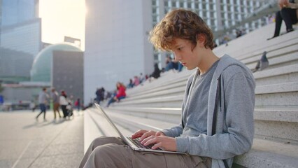 Concentrated young programmer freelancer looking at laptop screen, working remotely outdoor. Head shot focused smiling guy chatting in social network, typing message, internet web surfing