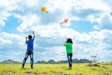 Back View Shot Of Teenager Kids Flying Kite On Top Of Mountain - Concept Of Weekend Holidays, Relaxation And Playful Childhood Lifestyles.