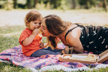 Wall Mural - Young beautiful mother with little baby boy eat pizza in park