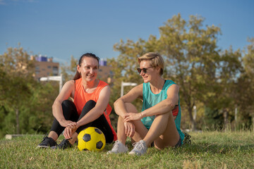 Two 30s years old woman on a training of soccer or European football in amateur team. Yellow ball, sport field with green grass.