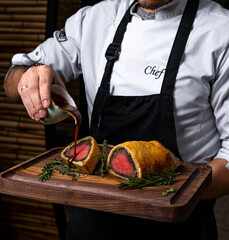 Wall Mural - meat baked in dough on a wooden board in the hands of a chef