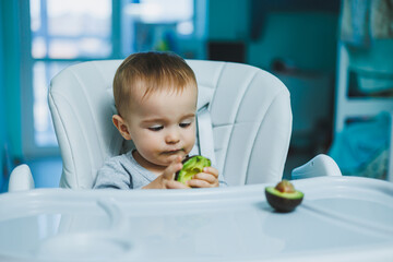 Little adorable baby eating avocado. Vitamin and healthy food for small children. Portrait of beautiful child of 8 months