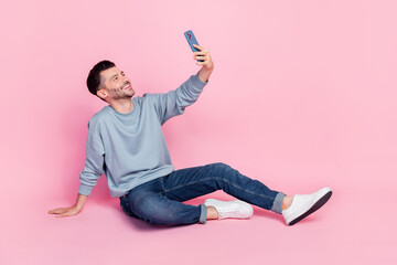 Sticker - Full length photo of attractive young man sit floor hold gadget make selfie wear stylish blue garment isolated on pink color background