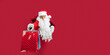 © ZaStock - Santa Claus looking through hole on red paper while holding shopping bags in hand. New Year shopping