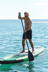 Young male surfer riding standup paddleboard in ocean.