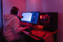 Woman Gamer Or Software Developer Sitting At The Modern Personal Computer And Eating Junk Food At Night In Room With Neon Lights