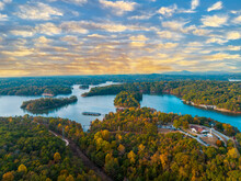 Lake Lanier In North Georgia, 4K Aerial Drone On A Sunny Fall Day. Radiant Clouds Both Blue And Orange. Clear View Of Fall Colored Trees And Blue Lake Water.
