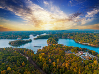 Lake Lanier in North Georgia, 4K aerial drone on a sunny fall day. Radiant clouds both blue and orange. Clear view of fall colored trees and blue lake water.