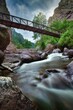 Vertical long exposure shot of a scenic river under a bridge in an evergreen forest