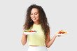 © Pixel-Shot - Happy young African-American woman with healthy and unhealthy food on light background. Diet concept