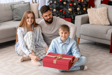 Wall Mural - Happy parents with their little son and Christmas present at home