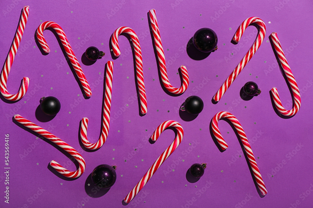 Composition with sweet candy canes and Christmas balls on purple background