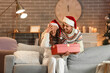 © Pixel-Shot - Young man surprising his beloved girlfriend with present at home on Christmas eve