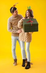 Canvas Print - Young couple in love opening Christmas gift on yellow background