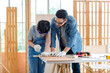 © Bangkok Click Studio - Asian professional male carpenter woodworker engineer dad in jeans outfit with safety gloves goggles helping teaching young boy son using handsaw cutting wooden stick in housing construction site