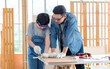 © Bangkok Click Studio - Asian professional male carpenter woodworker engineer dad in jeans outfit with safety gloves goggles helping teaching young boy son using handsaw cutting wooden stick in housing construction site