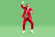 Happy guy having fun at New Year or Christmas party. Full body length portrait of funny cheerful joyful man in red suit and sunglasses dancing gangnam style on green studio background