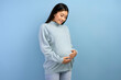 Image of a beautiful young pregnant asian woman smiling and looking at her belly